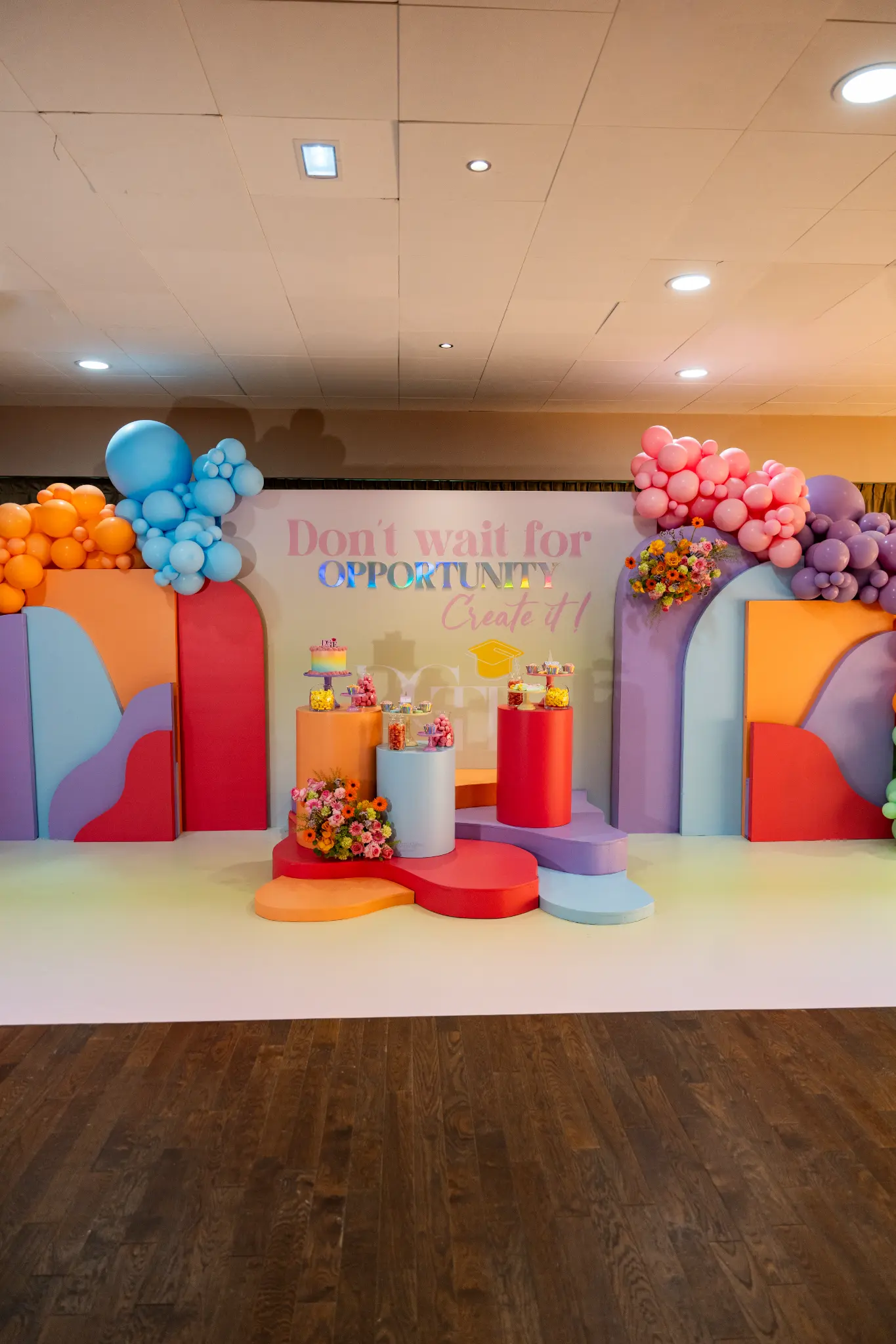 Scénographie événementielle immersive et colorée avec arches de ballons, panneaux graphiques, fleurs et présentoirs