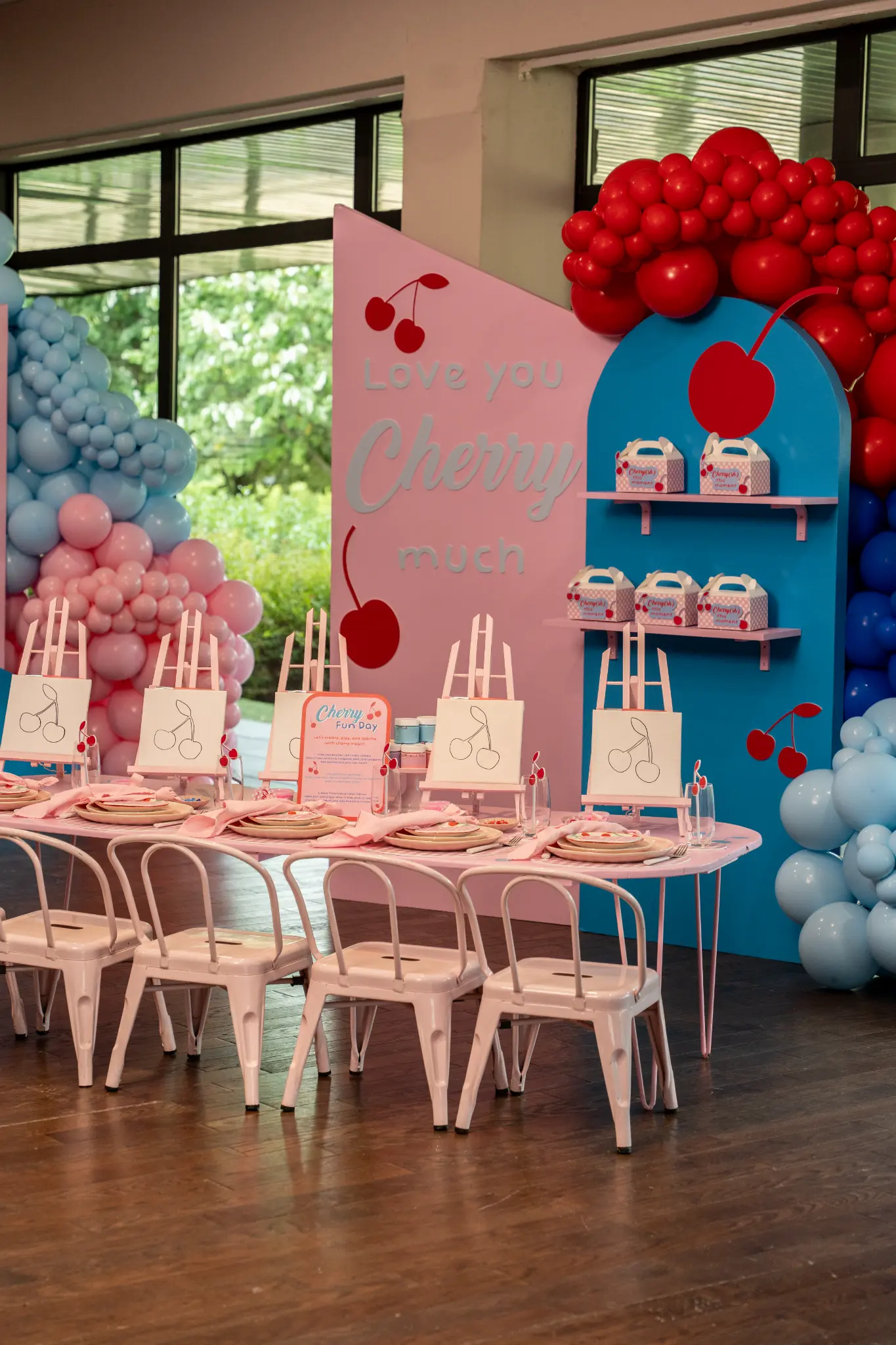 Kids Corner avec table goûter, petites chaises, présentoirs, fleurs et décor de ballons dans des tons bleus, rouges et roses